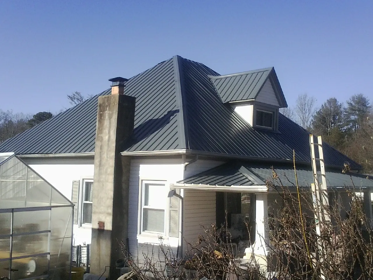 Dark blue standing seam metal roof on a white farmhouse with dormer — Slate & Tile Roof Repair by Roofing Brothers in Hewitt
