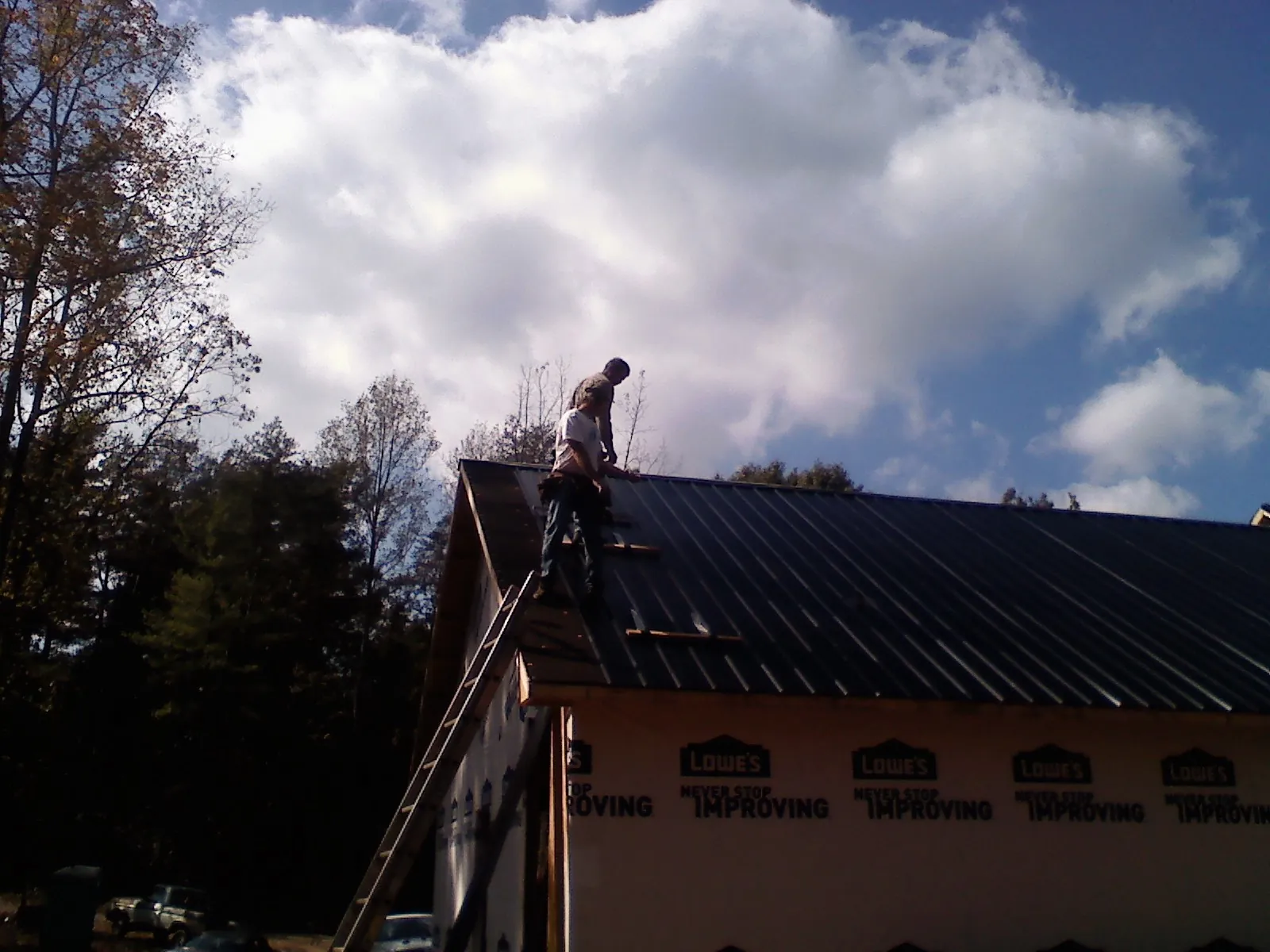 Roofer fastening dark metal panels high against a cloudy sky, from a Roof Inspection job in Hewitt