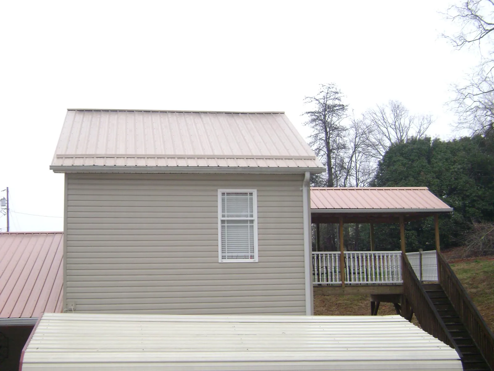 Tan metal roofs on a two story addition and attached porch, from a Roof Replacement job in Hewitt